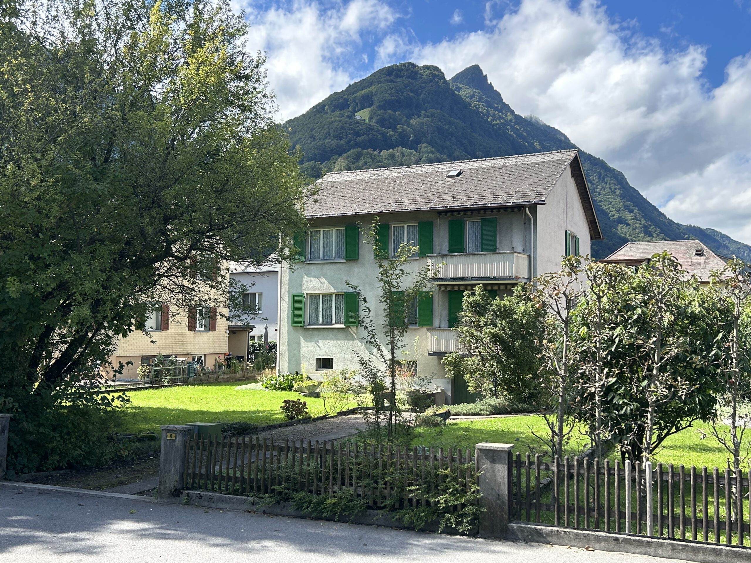 20250914_122022945_iOS Grosses, freistehendes 2-Familienhaus mit schönem Grundstück an sonniger, zentrumsnaher Lage in Niederurnen, Kanton Glarus Diese in die Jahre gekommene Liegenschaft liegt an einer kleinen Zufahrtstrasse im ruhigen Wohnquartier in kurzer Gehdistanz zum Zentrum. Einkaufsmöglichkeiten, ÖV-Anschlüsse und das Primarschulhaus befinden sich in unmittelbarer Nähe. Im Haus befinden sich zwei Wohnungen mit nahezu identischem Grundriss. Die Wohnung im Parterre verfügt über vier Zimmer, eine Küche und ein Bad mit Badewanne. In der Wohnung im Obergeschoss wurden zwei Zimmer zusammengelegt und renoviert. Somit bietet diese Wohnung neben einer Küche und einem Bad ein grosses Wohnzimmer und zwei Schlafzimmer.